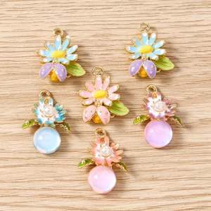 Détail de pendentifs fleurs et insectes en émail coloré avec perles sur fond de bois
