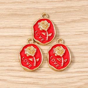 Macro detail of oval gold alloy charms with red enamel rose and LOVE engraving