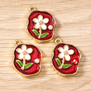 Makroaufnahme von Gold-Blumenanhängern mit roter Emaille und Perlen für DIY-Schmuckherstellung