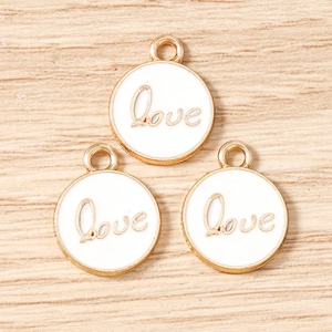 Detailed view of three white enamel Love pendants with gold borders for DIY jewelry making