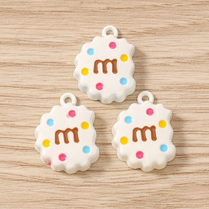 Détail macro de breloques en résine en forme de biscuit avec lettre M et points colorés DIY