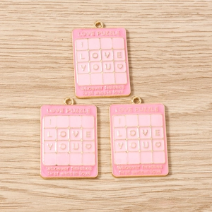 Detailaufnahme der rosa Emaille-Puzzle-Anhänger mit goldenem I LOVE YOU Design
