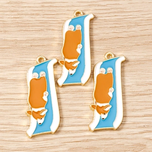 Detailed macro view of three enamel Corgi dog charms with golden plated edges on wood