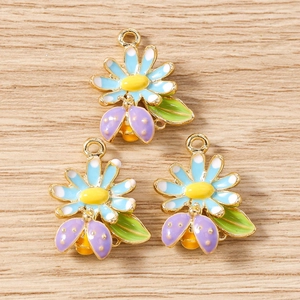 Détail des breloques bijoux DIY avec marguerites bleues et coccinelles sur fond bois