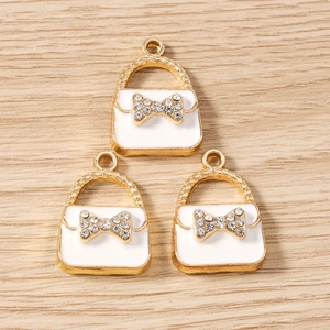 Detailed close-up of three handbag-shaped alloy pendants with enamel and bow rhinestones