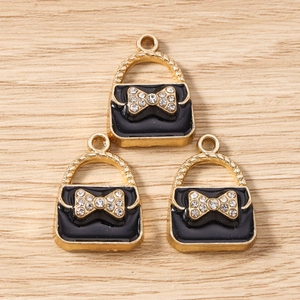 Close-up of golden handbag charms with black enamel finish and rhinestone bow details