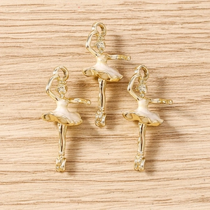 Detail of three golden ballet girl pendants with white enamel finish on a wood surface