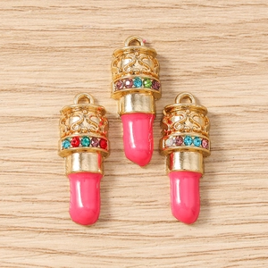 Macro-opname van drie gouden lippenstift bedeltjes met kleurrijke kristallen en email