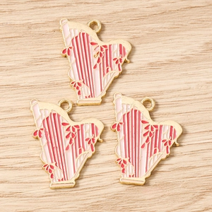 Detailed view of three pink and red enamel harp charms with gold plating for jewelry making