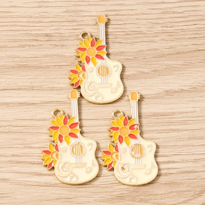 Detail of three sunflower guitar enamel charms with musical notes on wood background