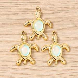 Vue macro de trois pendentifs tortue dorés avec incrustation d'opale sur fond de bois