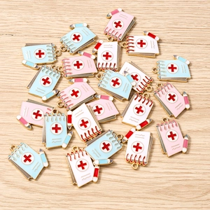 Macro detail of notebook-shaped enamel pendants with pencil and medical cross for DIY jewelry
