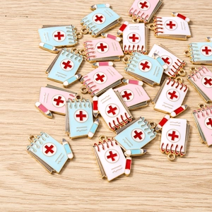 Detail view of medical notebook enamel charms in blue, pink, and white on a wood background