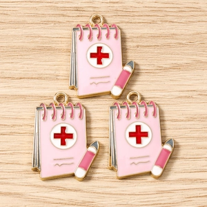 Macro detail of three pink medical notebook charms with red cross and golden metal edges