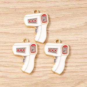 Detailed macro shot of three thermometer-shaped alloy pendants with gold plating and white enamel