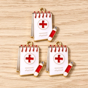 Detailed macro shot of white enamel medical notepad charms with red cross for DIY jewelry