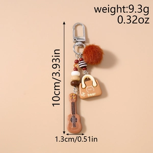 Detail of beaded keychain with brown pom pom, resin bear charm, and mini guitar pendant