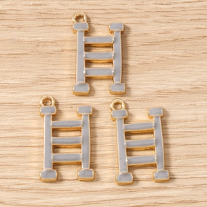 Close-up of three golden H-shaped charms with grey enamel inlay on a wood surface