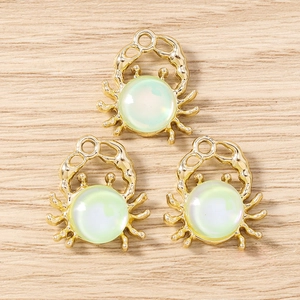 Detailed view of three golden crab charms with green stones on a wooden background