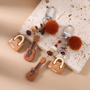 Detail view of a brown tassel keychain with beaded balls, mini guitar, and bear charm