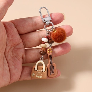 Detail of beaded keychain featuring a brown pompom, mini guitar, and bear bag charm