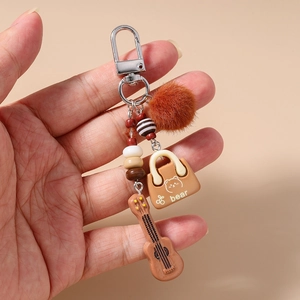 Detailed close-up of brown pompom guitar keychain with mini bear handbag charm