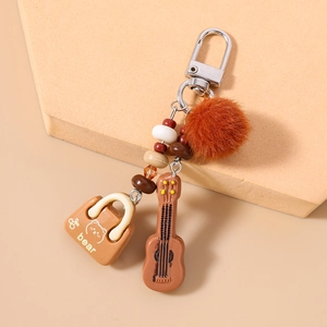 Detail view of guitar charm, mini bear bag, and plush ball on a brown beaded keychain