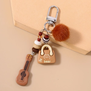 Close-up of brown plush ball keychain with a guitar charm and cartoon bear pendant