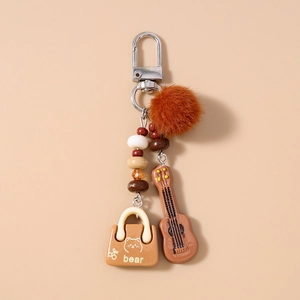 Close-up of guitar keychain with brown faux fur ball, resin ukulele and bear mini bag charm