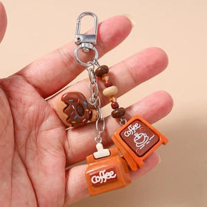 Detailed view of handmade coffee and donut keychain with charms held by hand