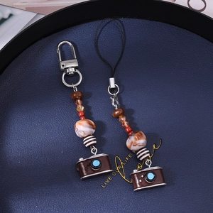 Detail of retro camera phone charm with brown beads and lobster clasp on blue tray