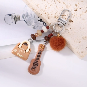 Detailed view of brown tassel keychain with mini bag, guitar pendant and plush pompom