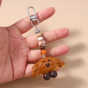 Close-up of cute croissant keychain with a smiley face, colorful beads, and silver metal clasp
