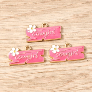 Detailed macro view of three pink cowgirl enamel charms with tiny white flower for DIY jewelry