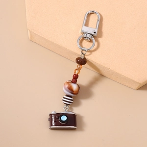 Detailed close-up of beaded phone strap featuring a vintage brown camera charm and earth tones