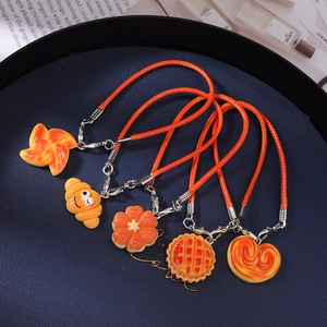 Flat lay of five orange braided rope food charm bracelets with croissants and fruit on blue tray