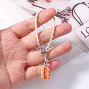 Close-up of orange grid cookie charm with cream woven lanyard and silver lobster clasp