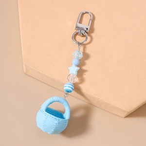 Detail of light blue beaded keychain with miniature basket and star charms on beige board