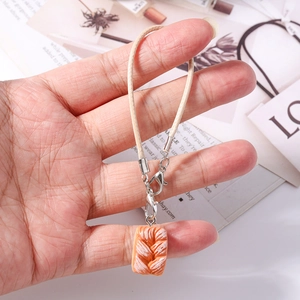 Detailed close-up of a realistic braided bread resin pendant on a cream woven phone strap