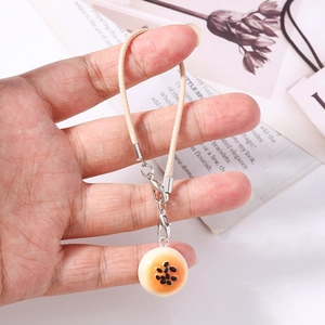 Macro shot of realistic miniature donut bread charm with woven lanyard held in hand