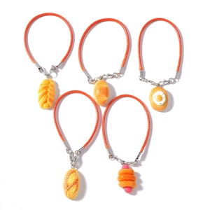 Detail of five woven orange bracelets featuring realistic resin bread and egg charms