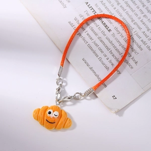 Detailed close-up of a realistic croissant charm with a cute face and orange woven strap