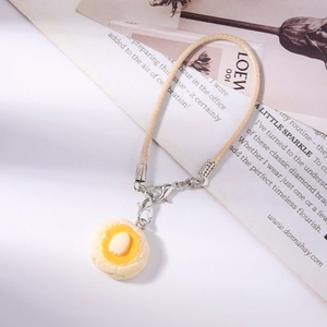 Close-up of realistic cream bagel and fried egg pendant with beige woven phone strap