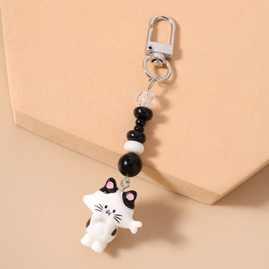 Close-up of white resin cat charm with black spots and faceted beads on silver lobster clasp