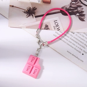 Gros plan du pendentif chocolat rose avec gravure MILK et dragonne de téléphone tissée