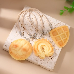 Detail view of miniature waffle and bread charms with woven lanyards on stone surface