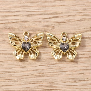 Detailansicht von zwei goldenen Schmetterlingsanhängern mit dunklen Herz-Edelsteinen für DIY