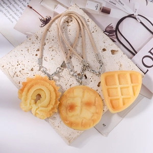 Detailed view of realistic waffle and bread charms with woven straps on a stone surface
