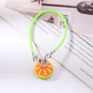 Detailed macro view of an orange fruit pendant on a vibrant green braided strap