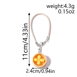 Macro detail of food pendant keychain with woven cord, showing weight and size specs